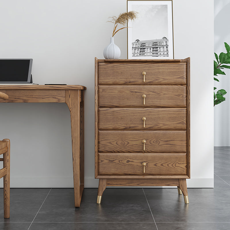 Wooden dresser with gold handles next to a desk in a room with a plant and framed picture on the wall.