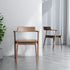 Two wooden chairs in a minimalistic room with a plant and white curtains.