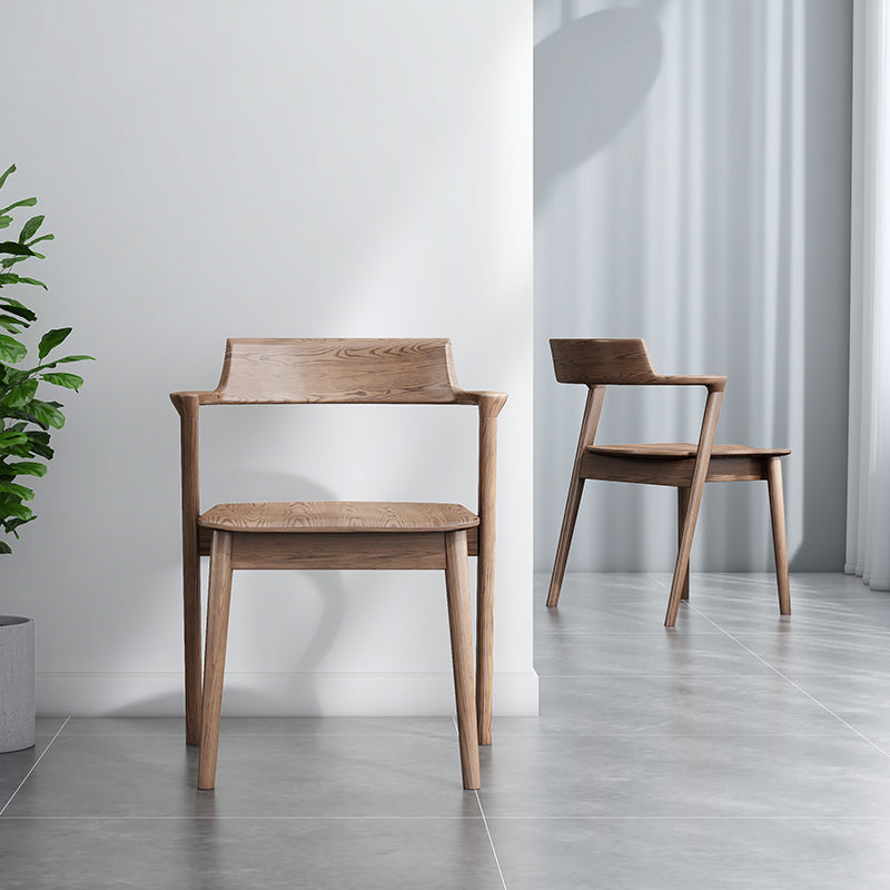 Two wooden chairs in a minimalistic room with a plant and white curtains.